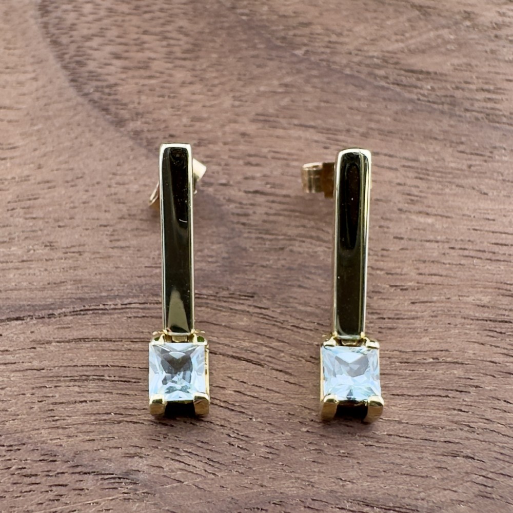 A pair of 9ct yellow gold drop stud earrings featuring vertical polished bars with square-cut light blue aquamarine stones at the base.