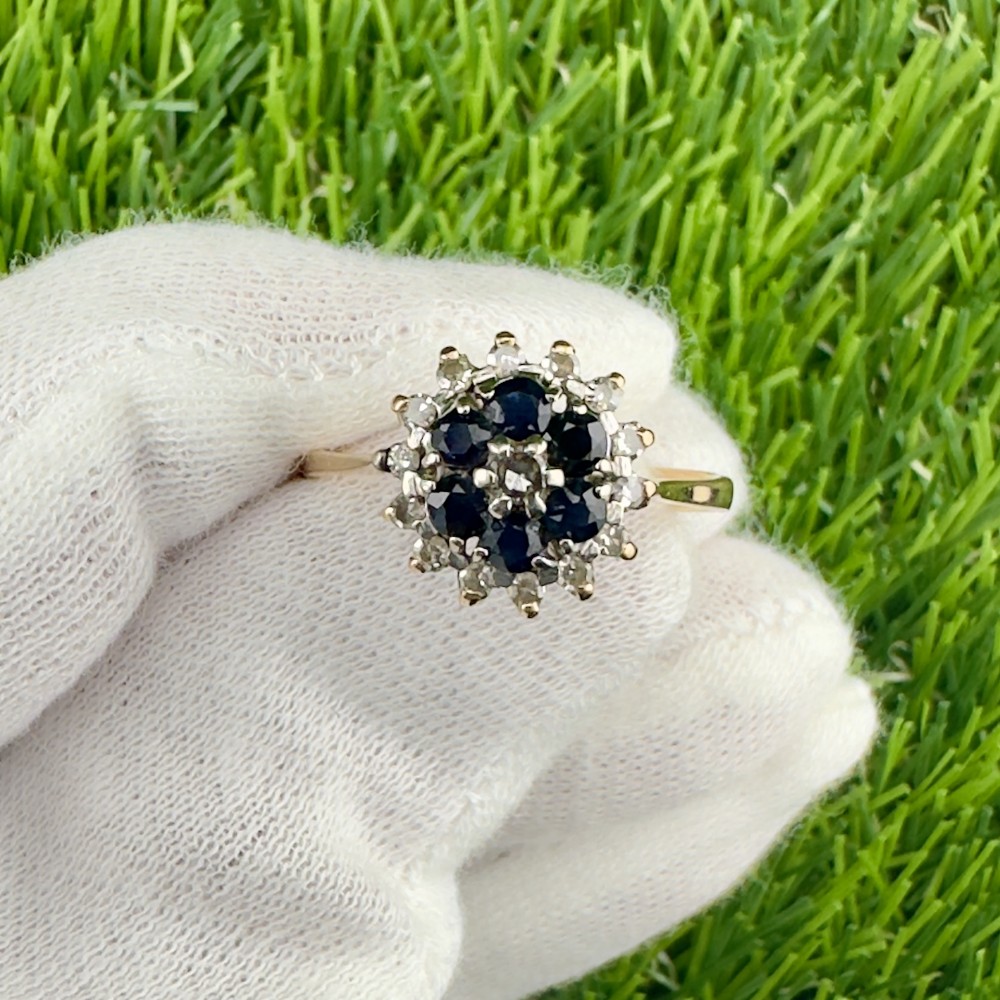 An 18ct yellow gold cluster ring set with round deep blue sapphires encircled by small diamond accents in a floral motif.