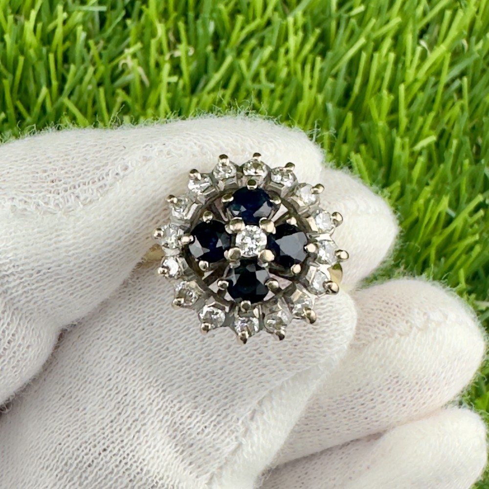 An 18ct gold ring featuring four central dark blue sapphires set in a cluster and surrounded by a outer halo of round diamonds.