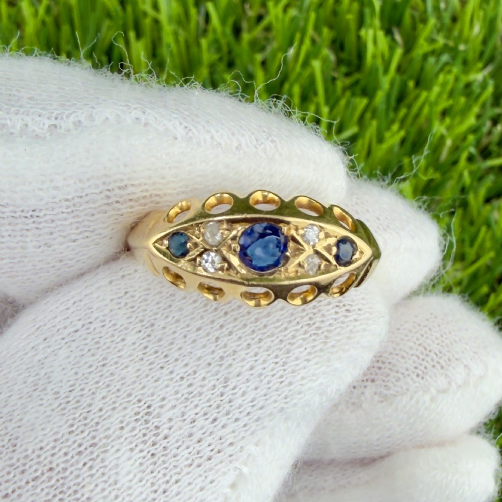 An 18ct yellow gold George V boat ring set with three blue sapphires and accent diamonds featuring an openwork carved gallery.