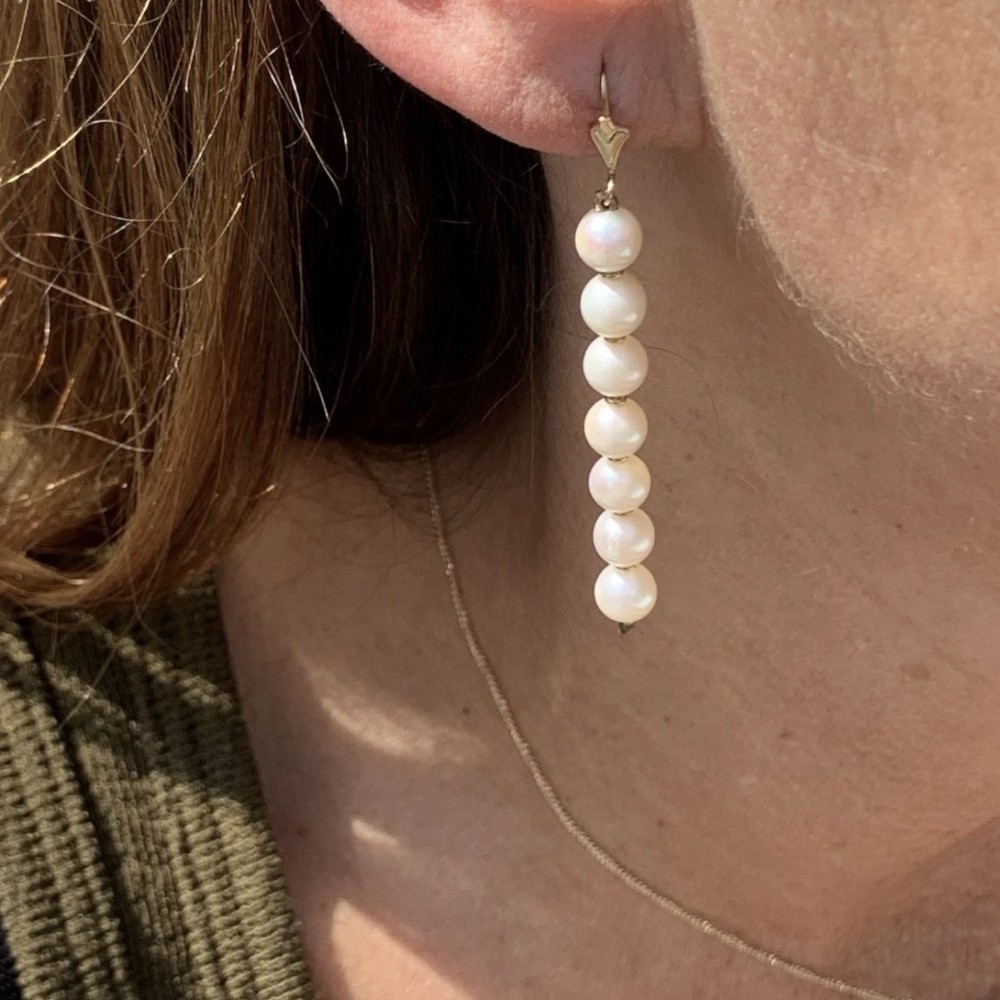 A vertical linear drop earring featuring seven round cream cultured pearls mounted on a 9ct gold fitting.