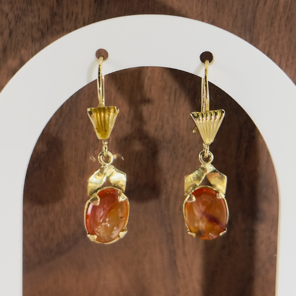 A pair of 18ct yellow gold drop earrings featuring oval carved orange agate cameos suspended beneath fan-shaped gold accents.