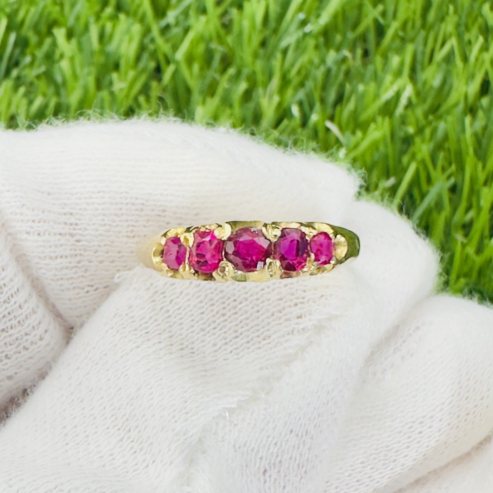 An 18ct yellow gold ring featuring five graduated cushion-cut rubies set across a carved setting.