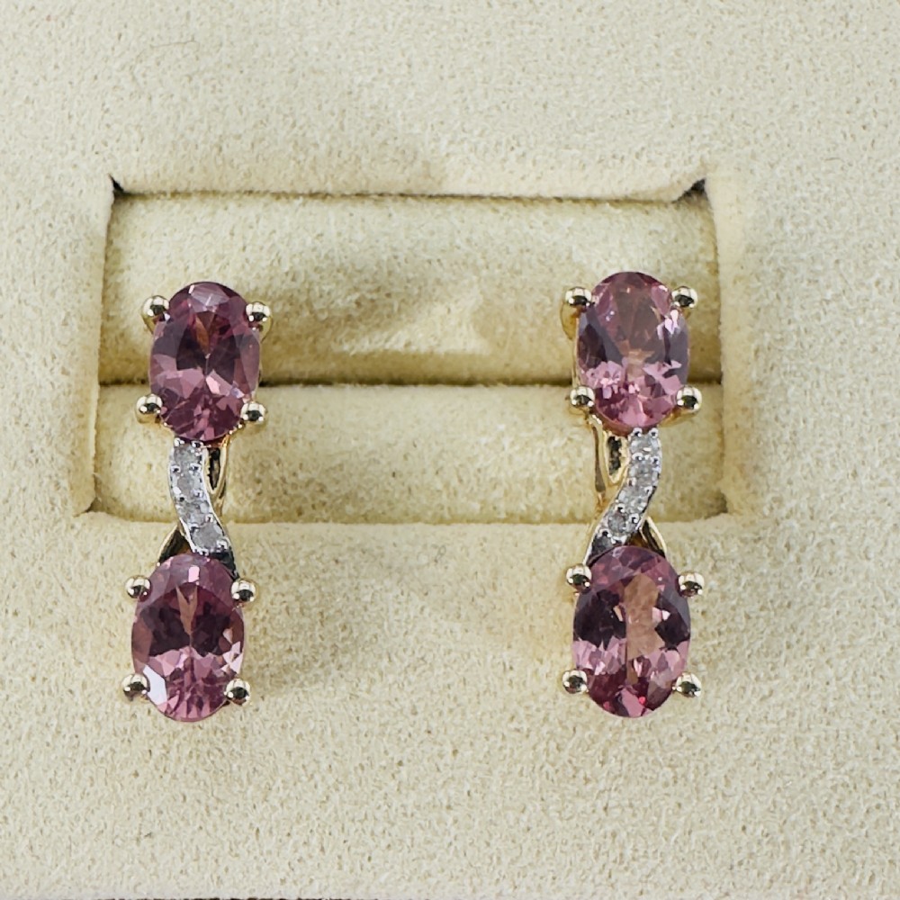 A pair of 9ct yellow gold drop earrings featuring two vertically arranged oval cut pink spinels connected by a diamond-set accent bridge.
