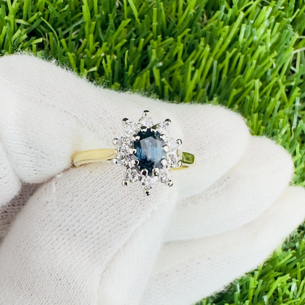 An 18ct gold cluster ring featuring a central oval blue sapphire surrounded by a starburst halo of small diamonds.