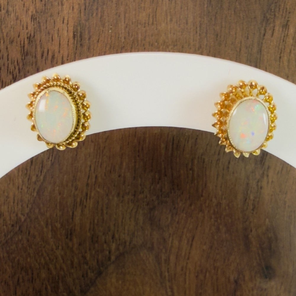 A pair of 9ct yellow gold stud earrings featuring central oval opal cabochons surrounded by textured gold rope borders.