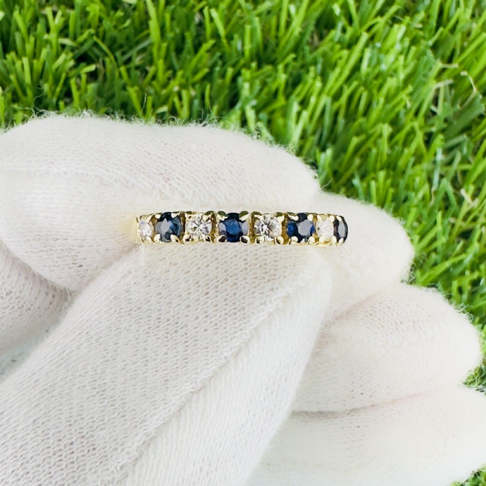 An 18ct yellow gold half eternity ring featuring an alternating row of four round blue sapphires and four round diamonds held in claw settings.