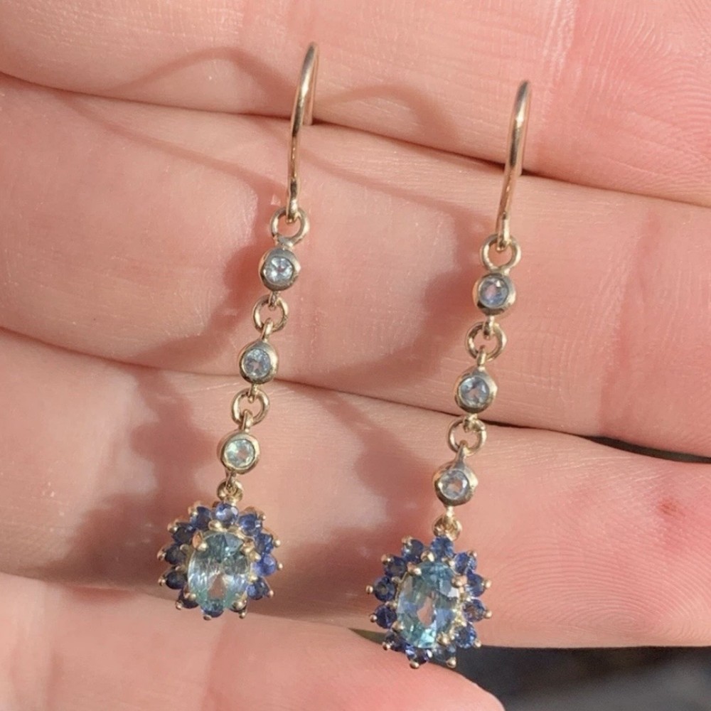 A pair of 9ct yellow gold drop earrings featuring vertically linked bezel-set gemstones terminating in oval blue and green sapphire cluster pendants.
