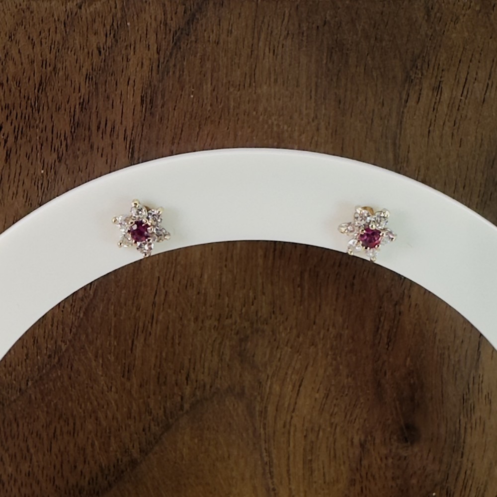 A pair of 9ct yellow gold cluster stud earrings featuring a central round red ruby framed by white zircon accent stones.