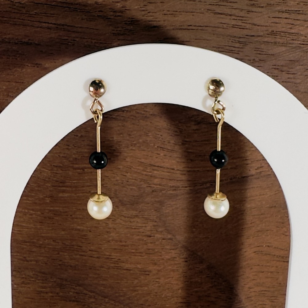 A pair of 9ct yellow gold drop earrings featuring ball studs, vertical wire links holding central black onyx beads, and cream pearl drops.