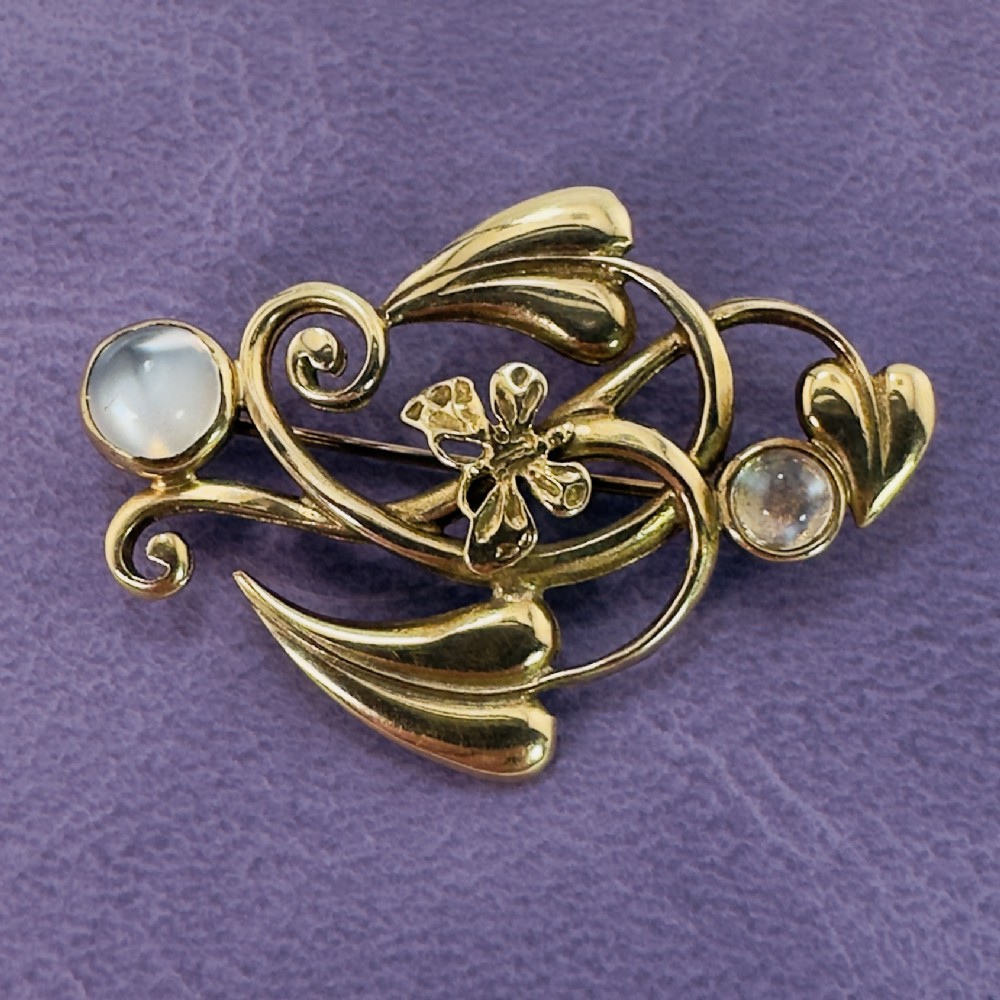 A 9ct gold Art Nouveau brooch featuring flowing whiplash leaves, a central butterfly motif, and two bezel-set round moonstones.