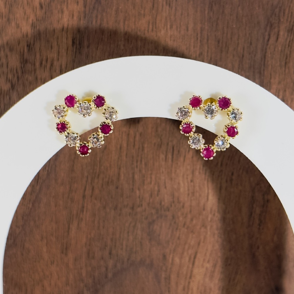 A pair of 9ct yellow gold heart-shaped stud earrings set with alternating round red rubies and clear white spinels.