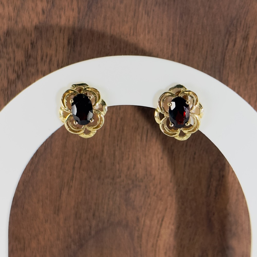 Pair of 9ct yellow gold stud earrings featuring oval deep red garnets framed by openwork floral borders.