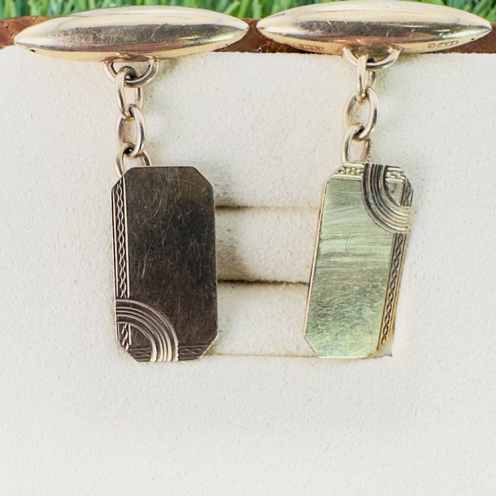 A pair of 9ct gold Art Deco cufflinks featuring rectangular faces with geometric corner engraving and chain link connectors.