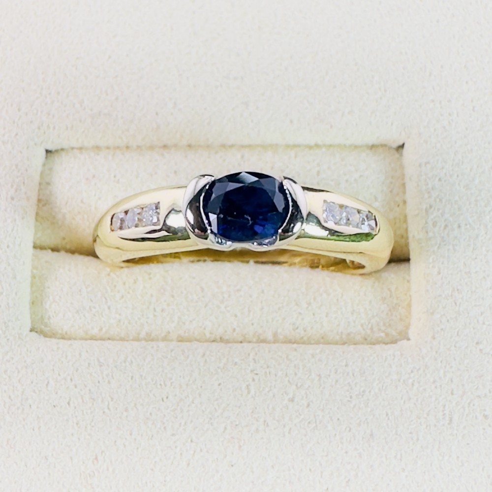 An 18ct yellow gold band ring with a central oval dark blue sapphire and small accent diamonds set into each shoulder.