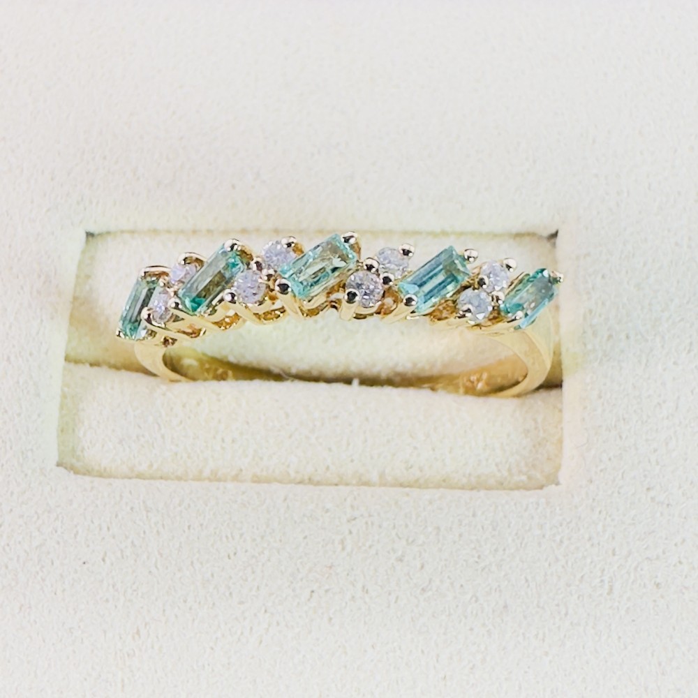 An 18ct yellow gold band featuring a row of diagonal baguette cut emeralds interspersed with small round brilliant diamonds.