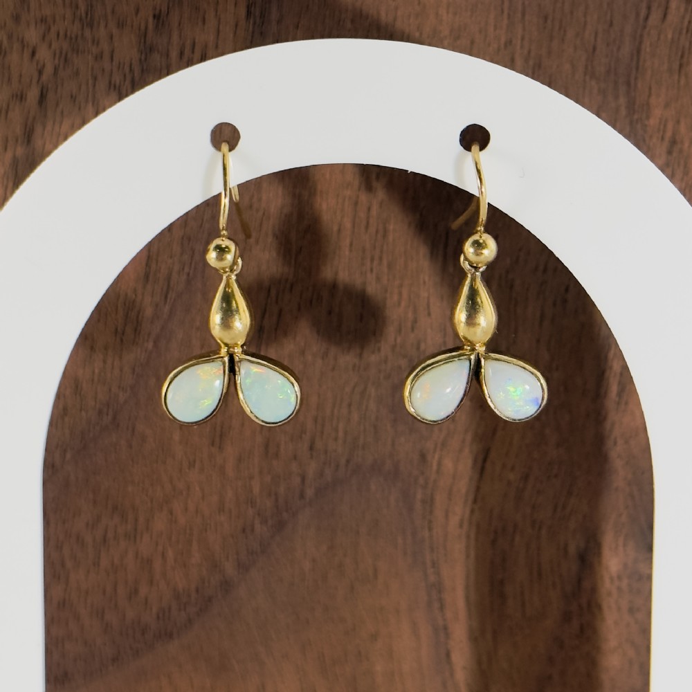 Pair of 9ct yellow gold drop earrings featuring twin pear-shaped white opal cabochons mounted below a teardrop gold accent with hook fittings.
