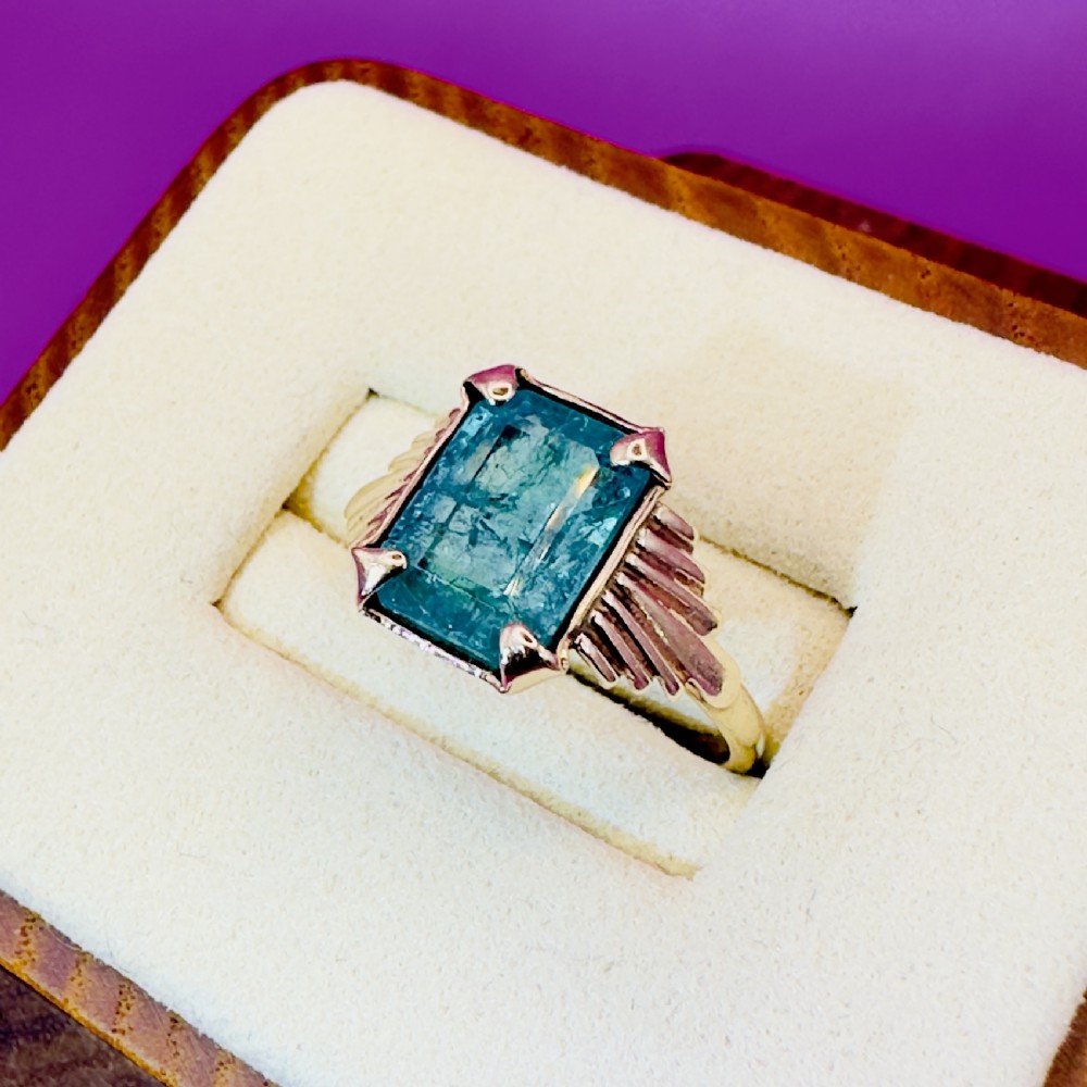 An Art Deco 9ct gold ring set with a central rectangular emerald featuring stepped fan-shaped shoulders.