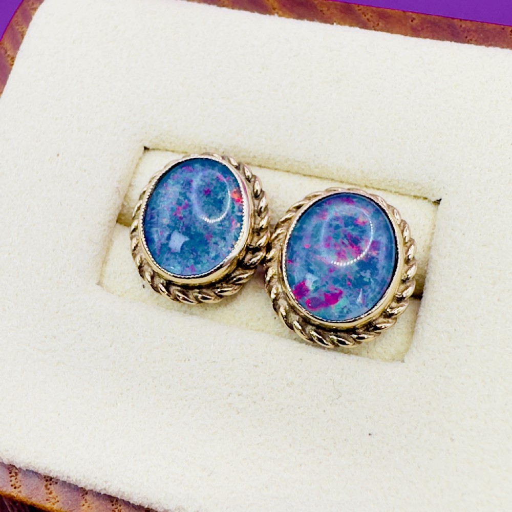 A pair of oval 9ct gold stud earrings set with iridescent black opal doublets and bordered by a twisted rope pattern.