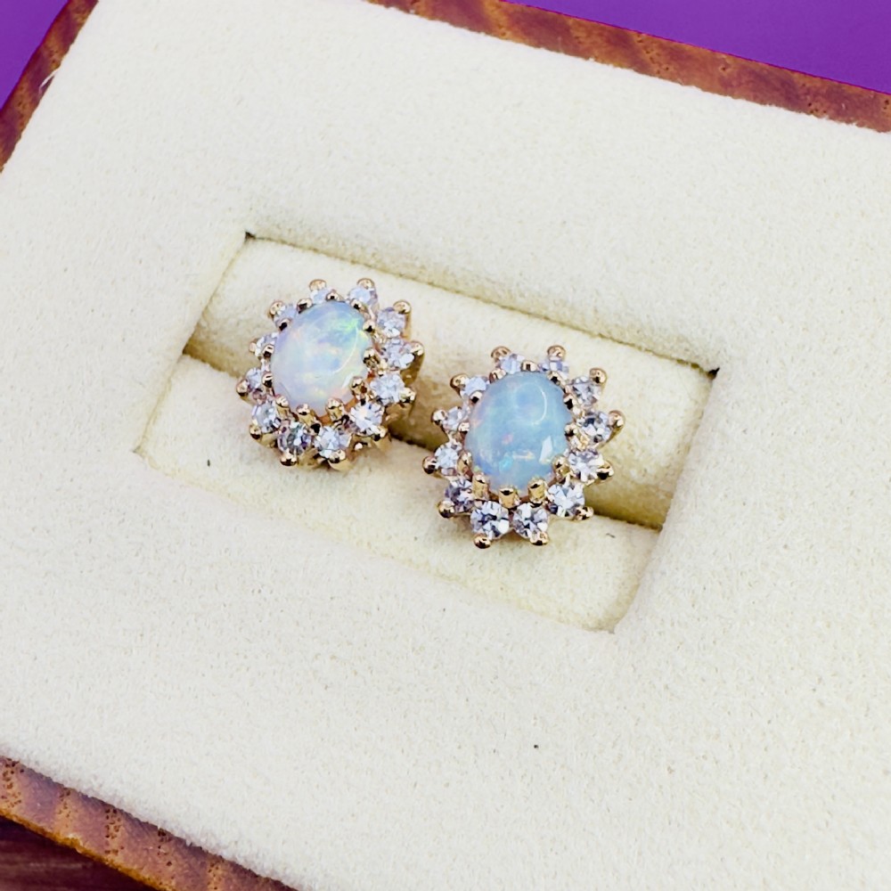Pair of 9ct yellow gold stud earrings featuring central oval cabochon opals surrounded by a halo cluster of small diamonds.