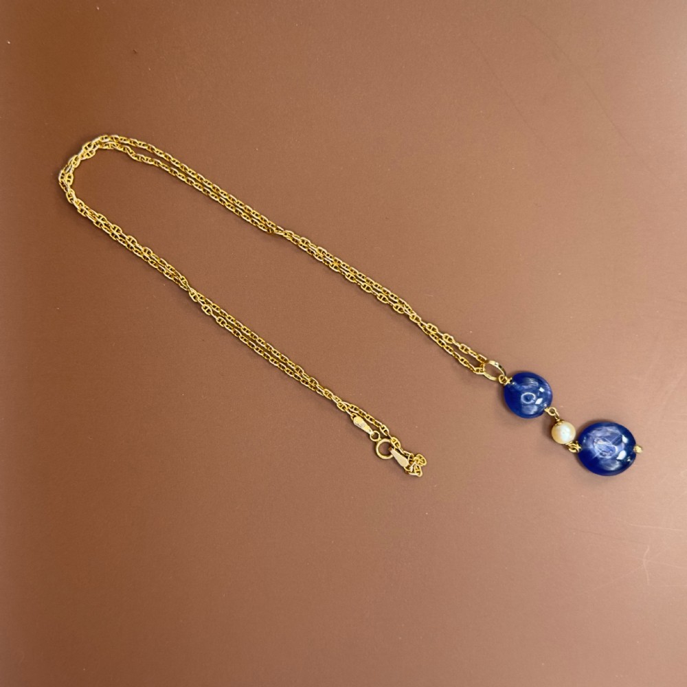An 18ct yellow gold pendant featuring two round disc-shaped cabochon blue sapphires linked by a central white pearl. View XI