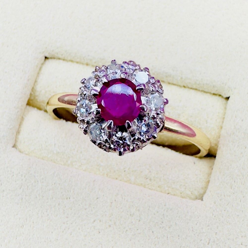 An 18ct yellow gold Art Deco cluster ring featuring a central round ruby surrounded by a halo of diamonds.