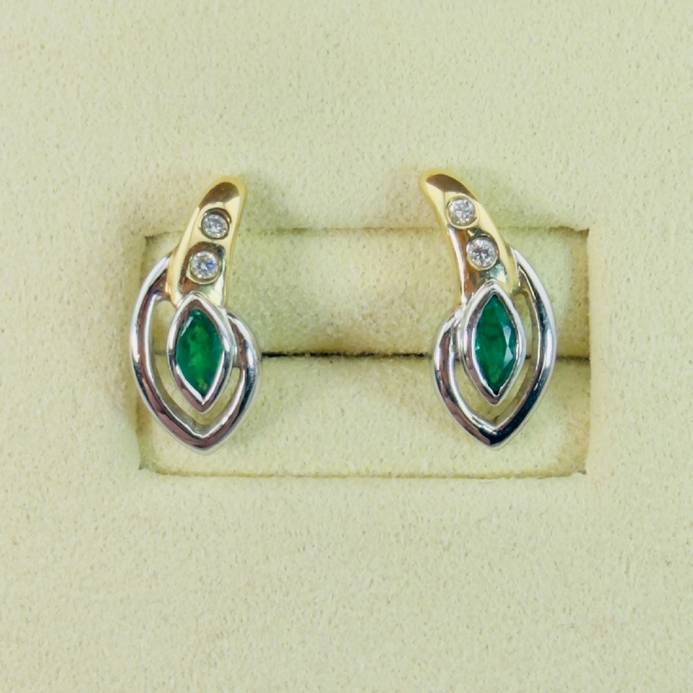 A pair of two-tone 14ct gold stud earrings, each featuring a central marquise-cut green emerald framed by a white gold curve and set with two small round diamonds.