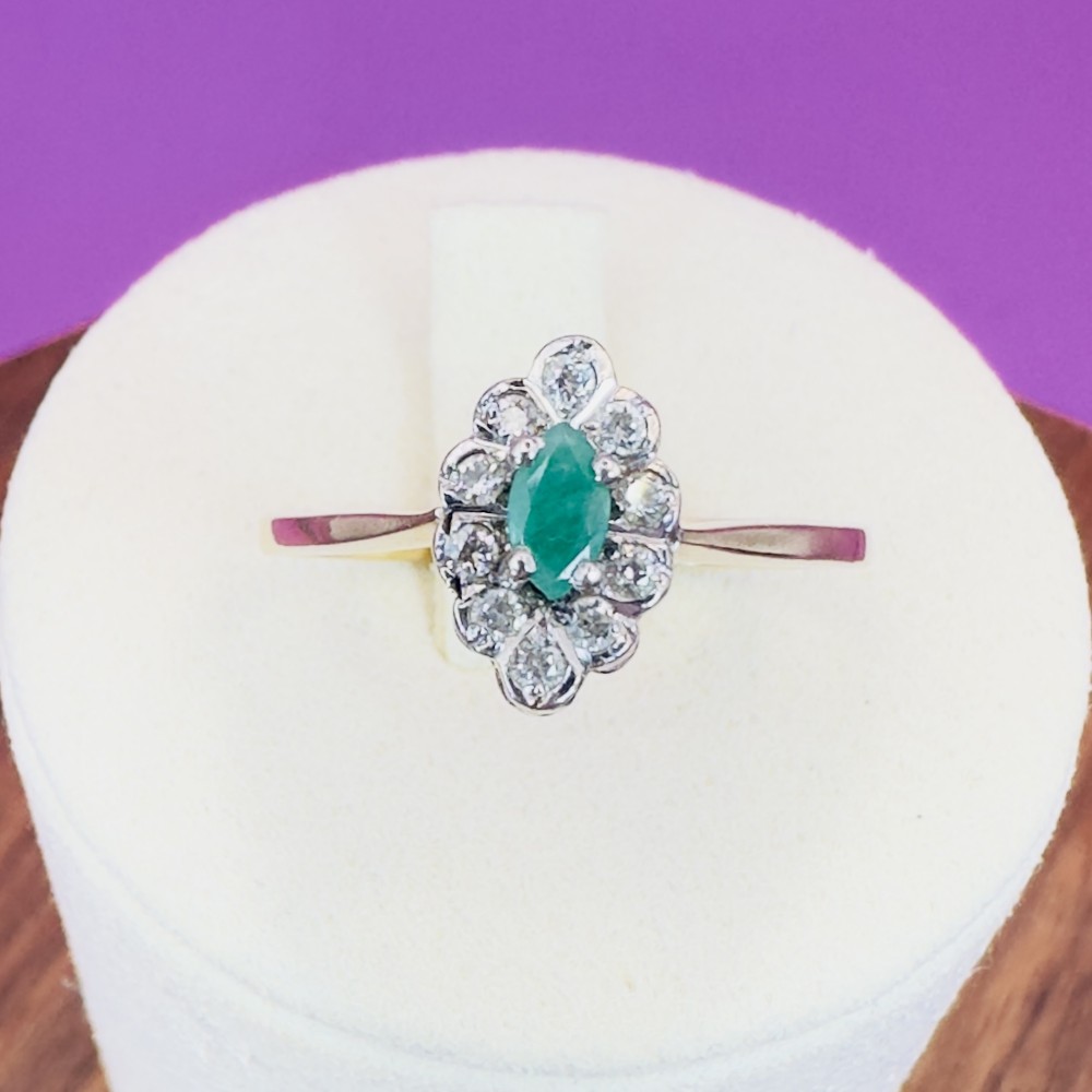 A 9ct yellow gold ring set with a central marquise-cut green emerald surrounded by a cluster halo of round diamonds.