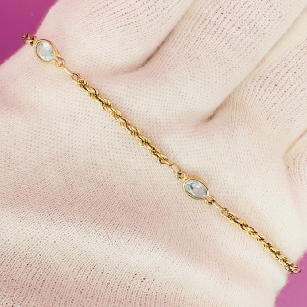A 9ct yellow gold rope twist chain bracelet featuring three bezel-mounted oval blue topaz gemstones.