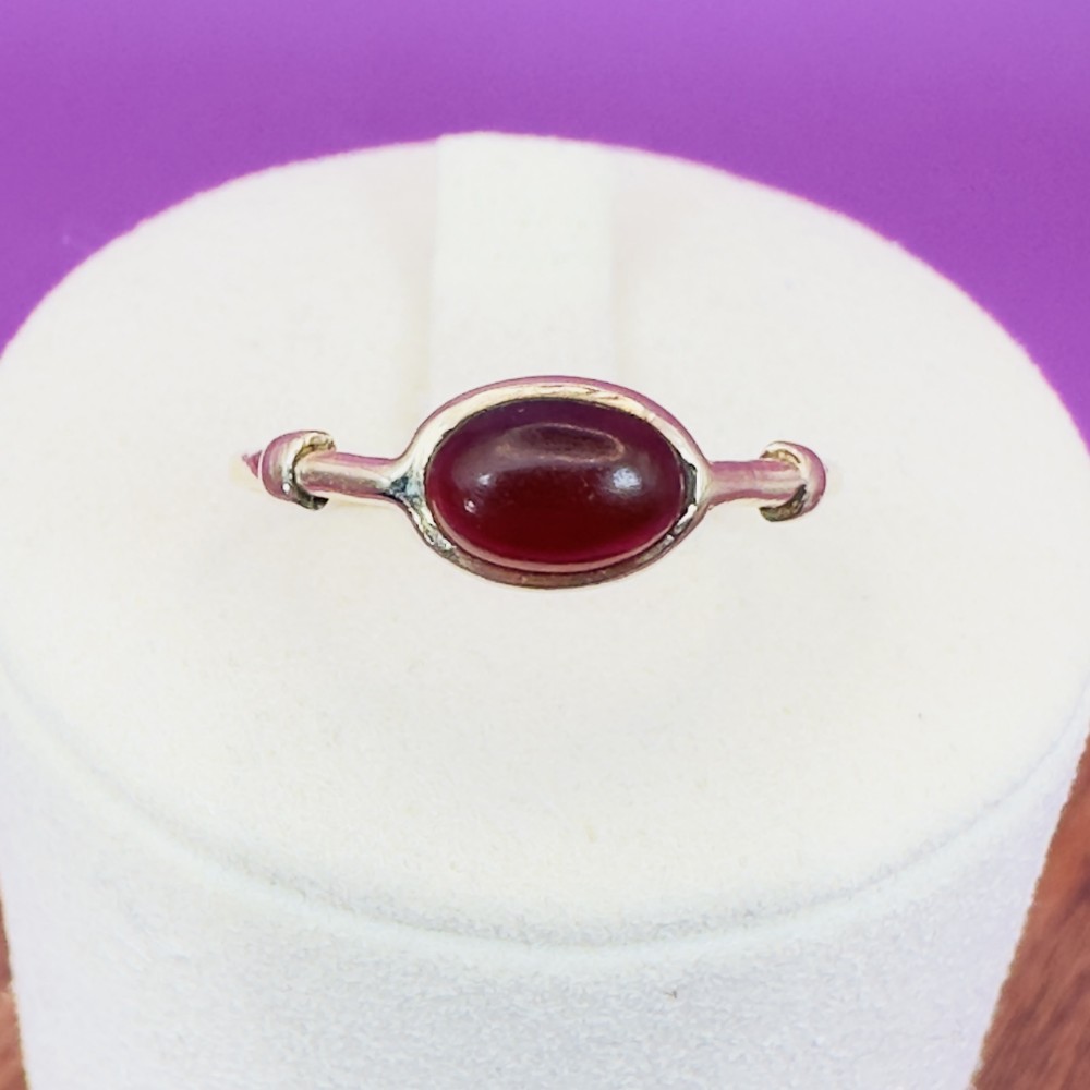 A Georgian 9ct gold solitaire ring featuring a smooth, oval red carnelian cabochon set in a bezel setting with subtle shoulder detail.
