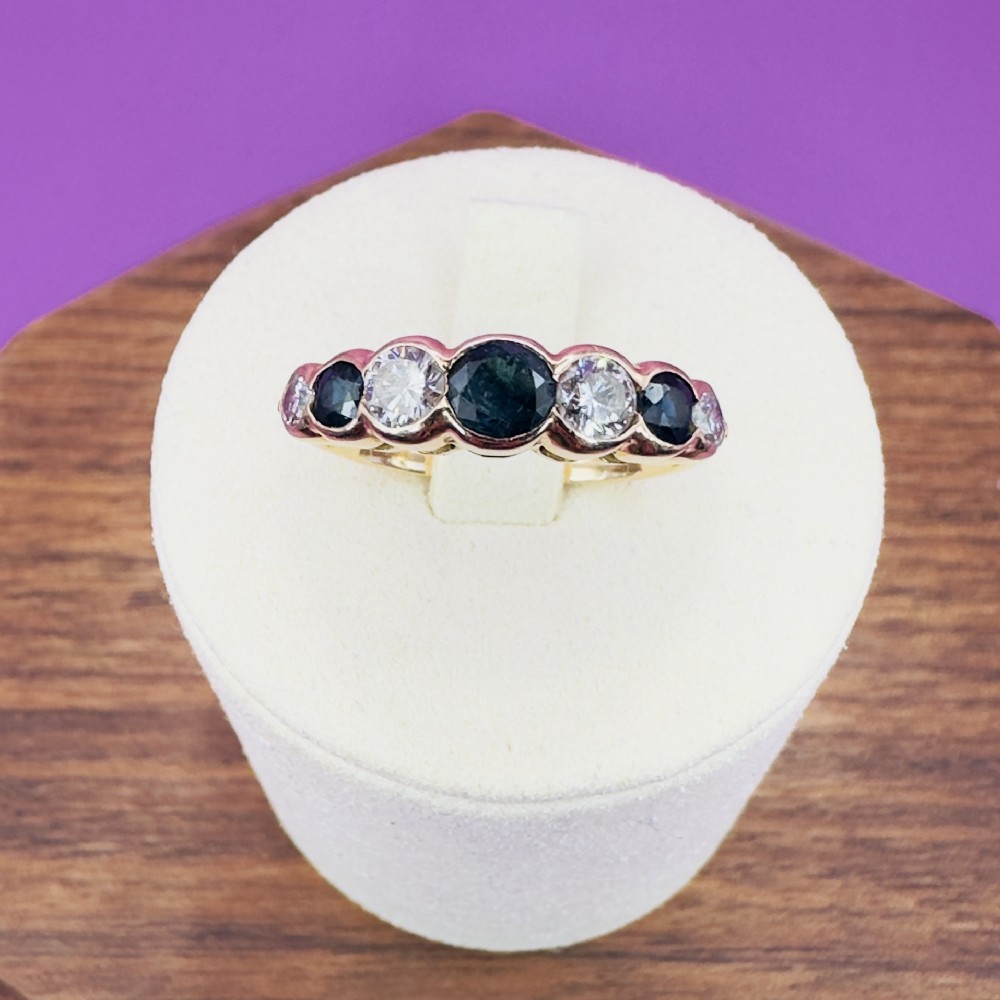 An 18ct yellow gold half eternity ring featuring seven alternating set sapphires and diamonds across the band.