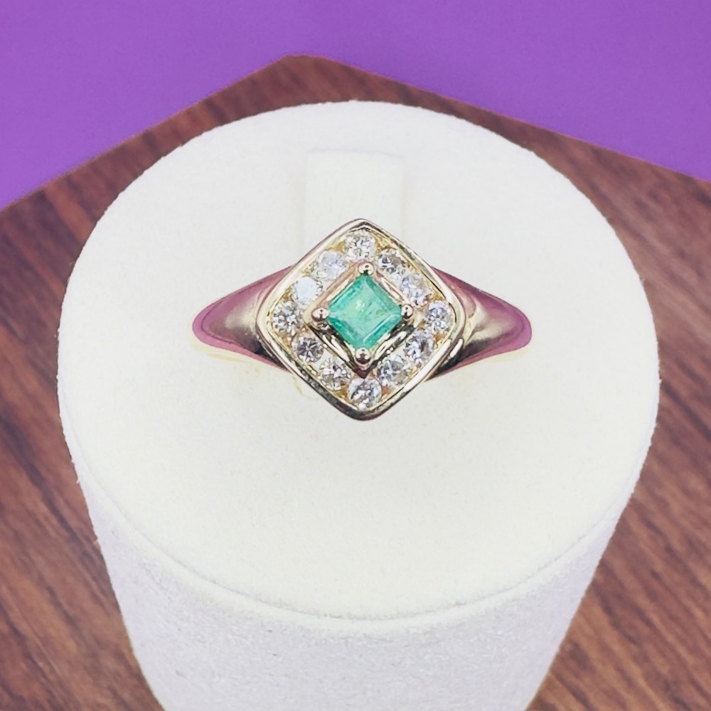 An 18ct yellow gold ring featuring a central square princess cut green emerald surrounded by a diamond halo cluster.