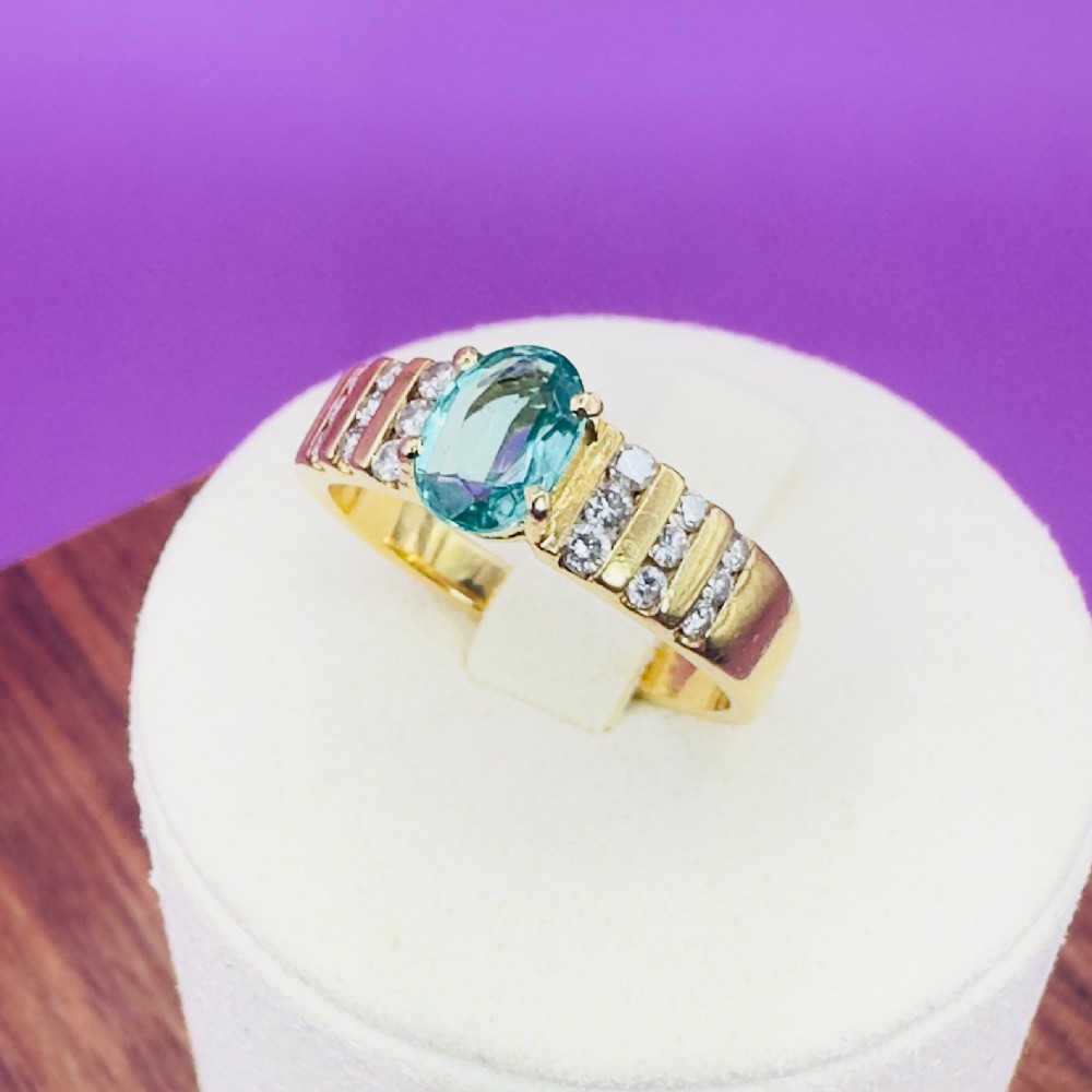 An 18ct yellow gold ring featuring a central oval-cut light green gemstone flanked by channel-set diamonds along a ridged band.