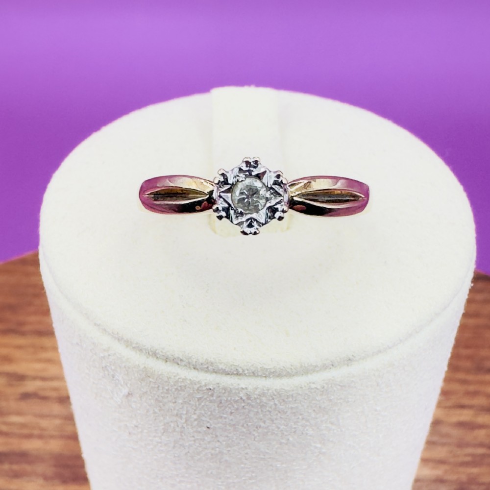 A 9ct yellow gold ring featuring a central round diamond set within a starburst illusion mount with carved shoulders.