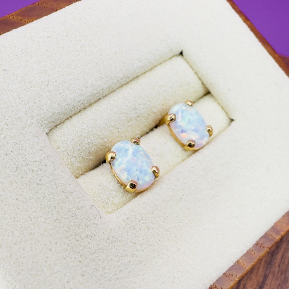 A pair of oval-cut white opal stud earrings mounted in four-claw 14ct yellow gold settings.