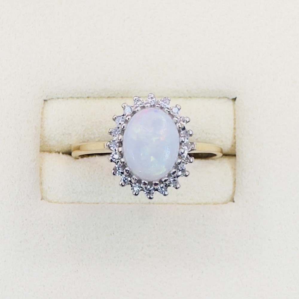 An oval cabochon opal framed by a halo of diamonds on a slim yellow gold band.