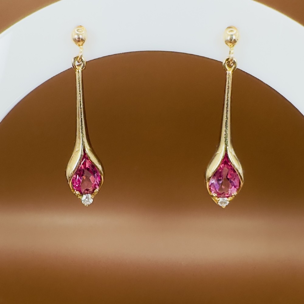 A pair of 9ct yellow gold drop earrings featuring sleek elongated mounts holding pear-cut pink topaz gemstones with small white topaz accents at the base.
