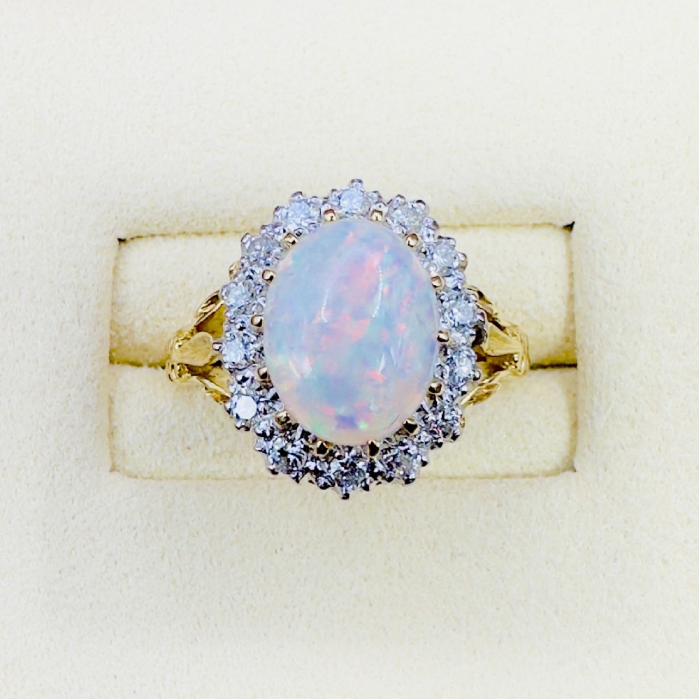 An 18ct gold ring featuring a central oval cabochon opal framed by a halo of brilliant-cut diamonds with carved shoulders.