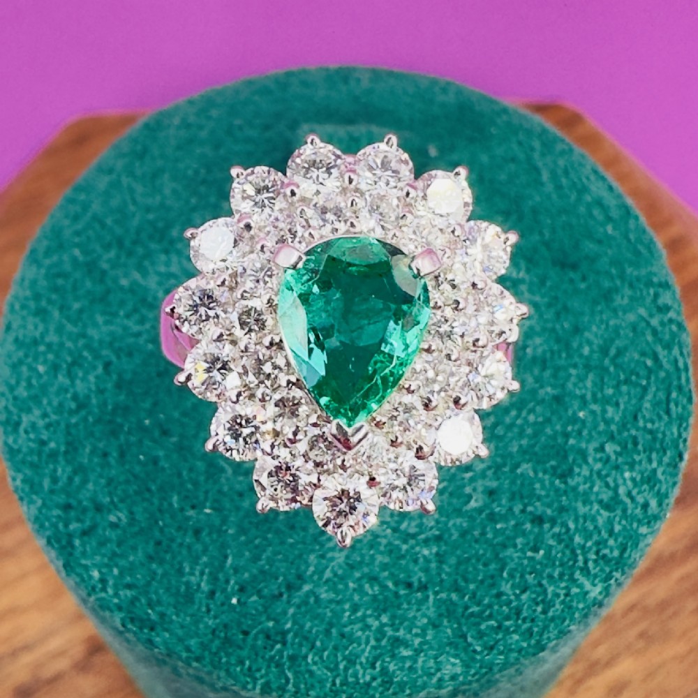 A platinum cluster ring set with a pear cut green emerald surrounded by a double halo of round diamonds.