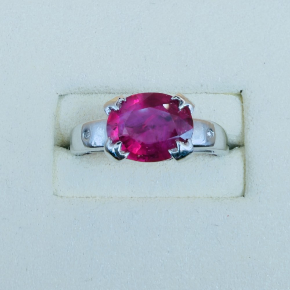 An 18ct white gold ring featuring a prominent oval cut red ruby secured by four corner claws, accented with small diamonds on the shoulders. View II