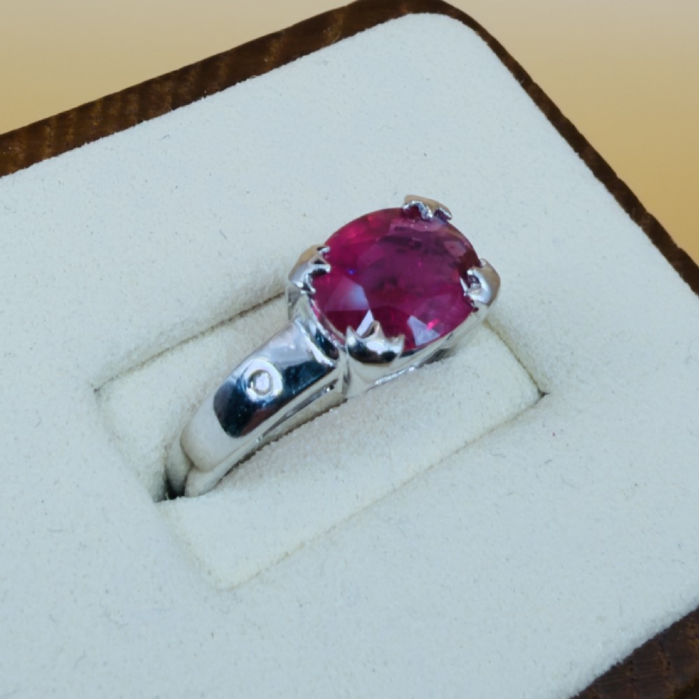 An 18ct white gold ring featuring a prominent oval cut red ruby secured by four corner claws, accented with small diamonds on the shoulders. View IV