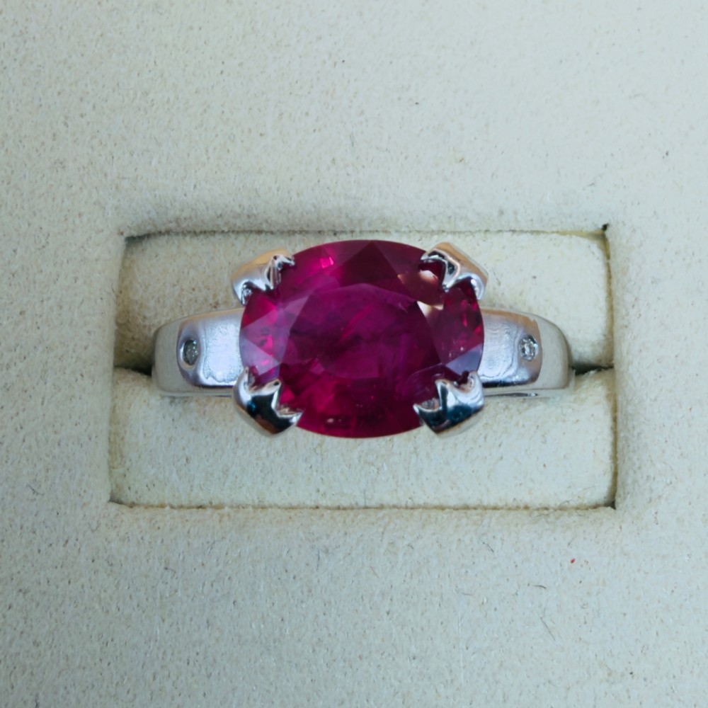 An 18ct white gold ring featuring a prominent oval cut red ruby secured by four corner claws, accented with small diamonds on the shoulders. View V