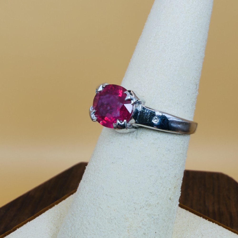 An 18ct white gold ring featuring a prominent oval cut red ruby secured by four corner claws, accented with small diamonds on the shoulders. View VII