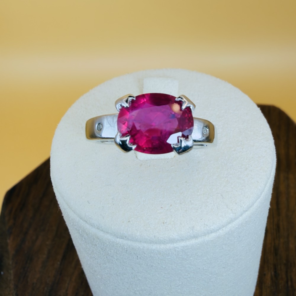 An 18ct white gold ring featuring a prominent oval cut red ruby secured by four corner claws, accented with small diamonds on the shoulders.