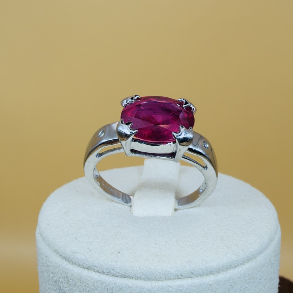 An 18ct white gold ring featuring a prominent oval cut red ruby secured by four corner claws, accented with small diamonds on the shoulders. View IX