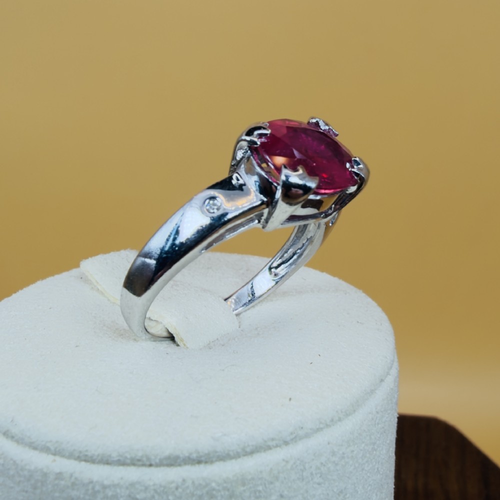 An 18ct white gold ring featuring a prominent oval cut red ruby secured by four corner claws, accented with small diamonds on the shoulders. View X
