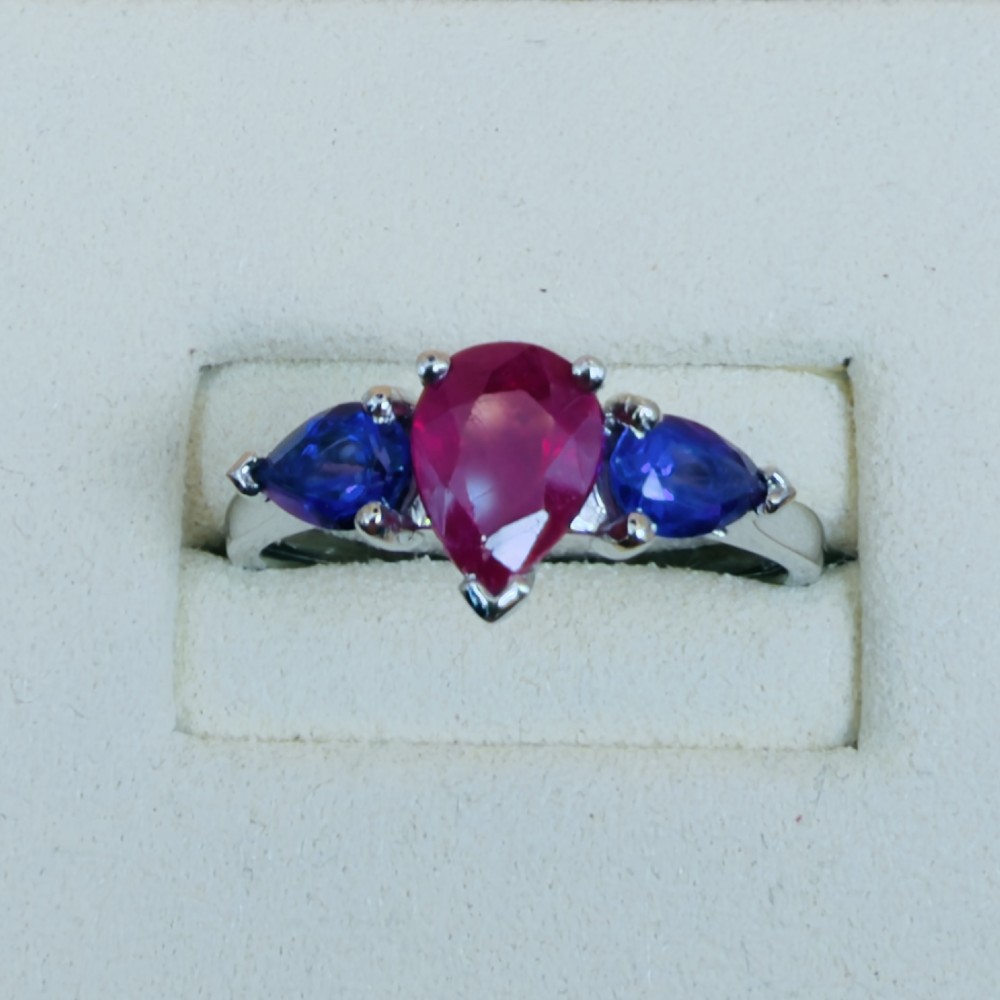 A platinum three-stone ring featuring a central pear-cut red ruby flanked by two pear-cut purple amethysts. View II