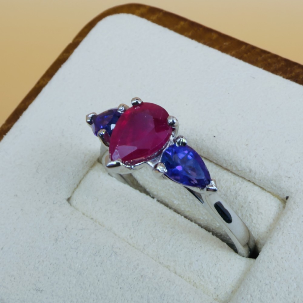A platinum three-stone ring featuring a central pear-cut red ruby flanked by two pear-cut purple amethysts. View III