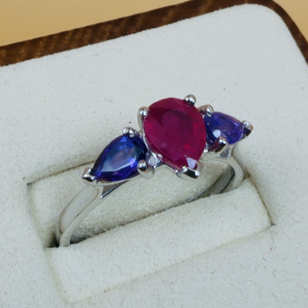 A platinum three-stone ring featuring a central pear-cut red ruby flanked by two pear-cut purple amethysts. View IV