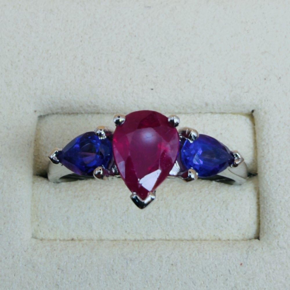 A platinum three-stone ring featuring a central pear-cut red ruby flanked by two pear-cut purple amethysts. View V